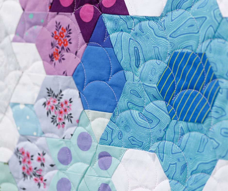 close-up of a vibrant english paper pieced design using a variety of shapes like hexagons, triangles, and diamonds.
