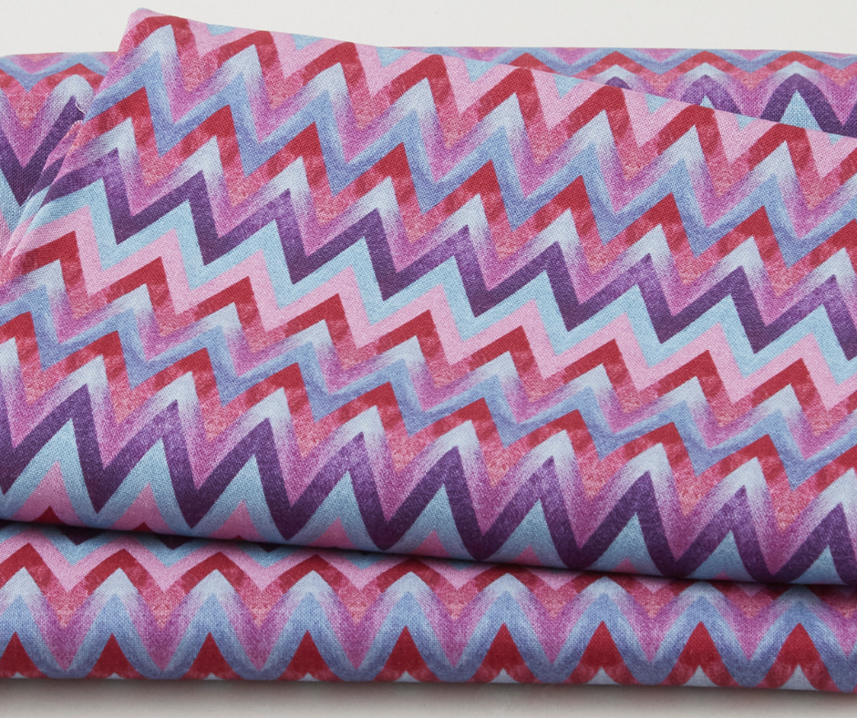 Colorful chevron-patterned fabric with zigzag stripes in red, pink, purple, and blue, folded neatly, creating a vibrant and lively texture.