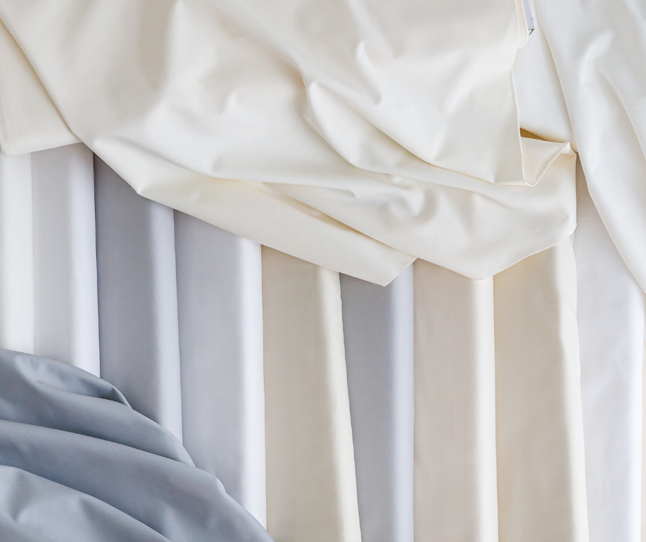 a selection of neutral colored fabrics arranged in a pleasing manner. some cotton fabrics are on bolts and there are a few fabrics that are draped across them.