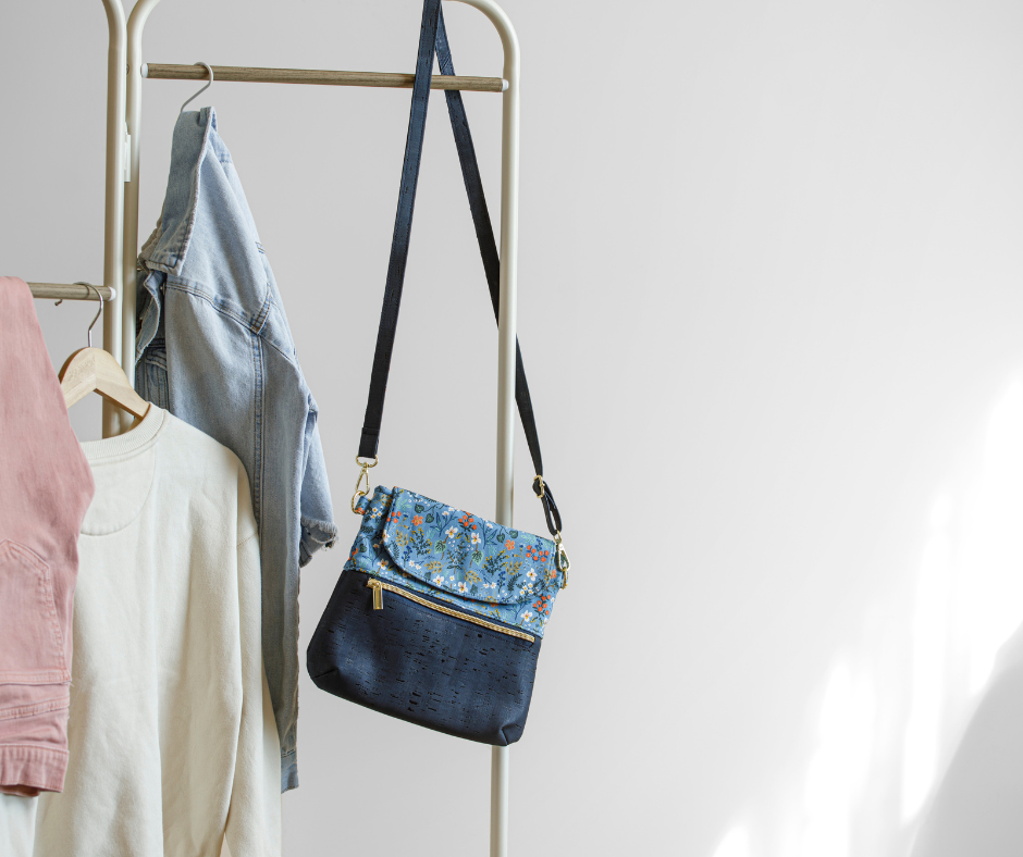 A floral-patterned handbag hangs on a clothing rack beside a light denim jacket and pastel sweaters, creating a casual and stylish vibe.