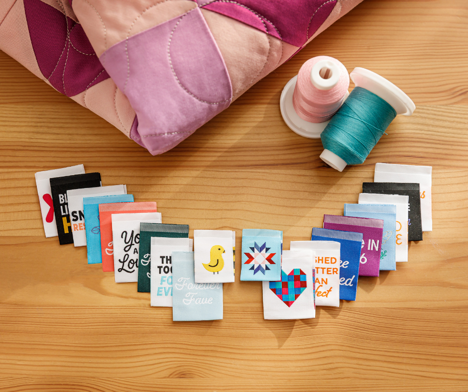 a colorful selection of quilt labels arranged on a wooden table with thread spools and a folded quilt.