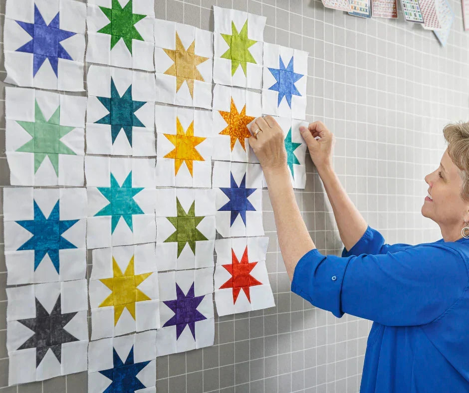 A smiling woman arranged colorful quilt blocks on a gridded design wall.