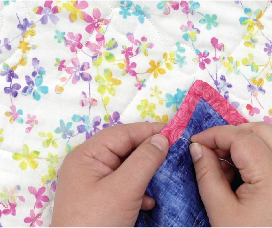 a pair of hands sewing binding onto the back of a colorful quilt.