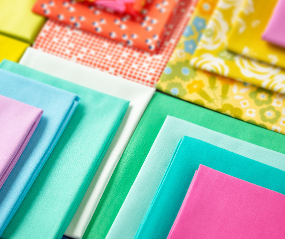 a collection of brightly colored fat quarter fabrics in solids and prints, neatly folded and arranged.