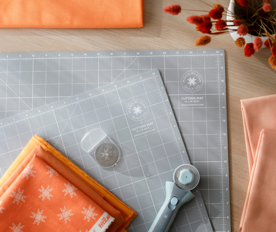 Colorful folded fabric and a rotary cutter on a cutting mat, placed on a wooden table.