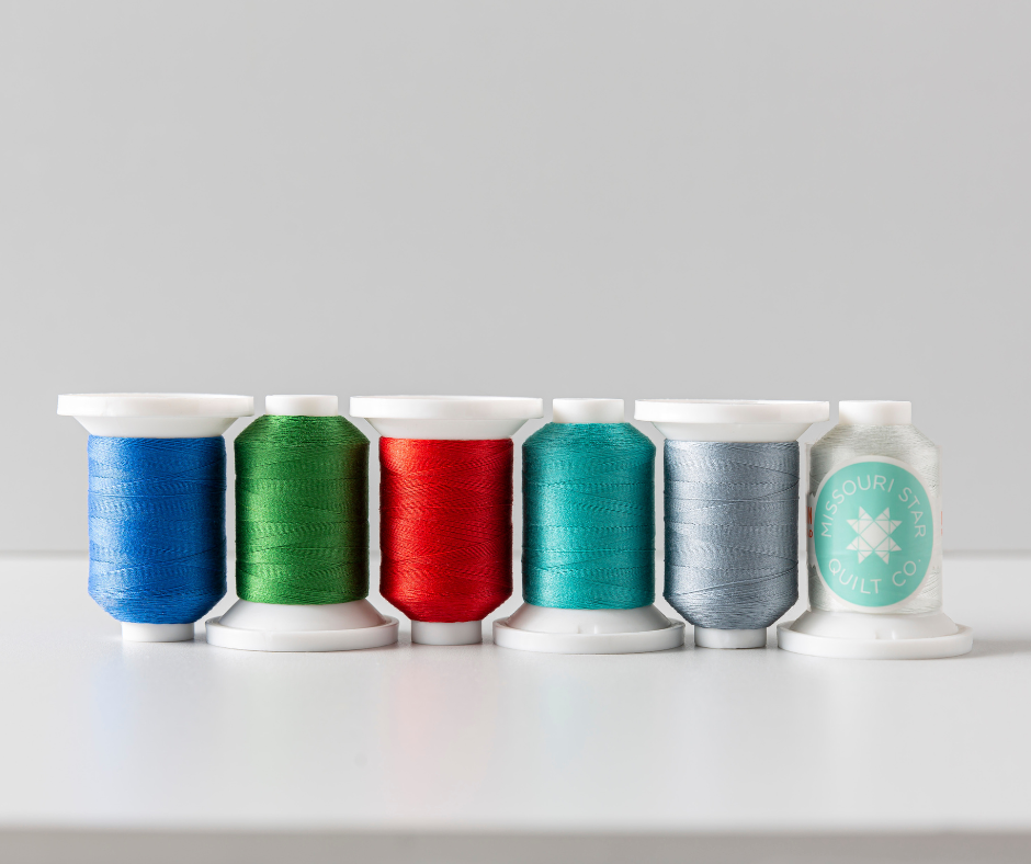 Five spools of thread in blue, green, red, teal, and gray are neatly aligned on a white surface, with a subtle gray background, evoking a calm, organized feel.