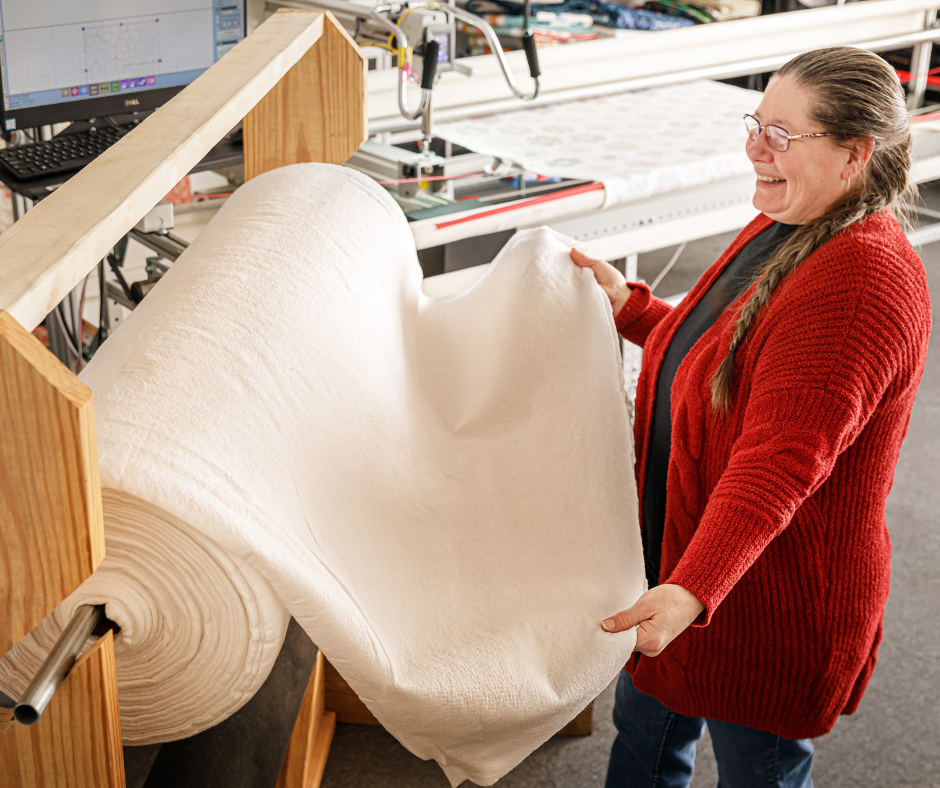 a smiling woman holds one end of quilt batting from a large roll.