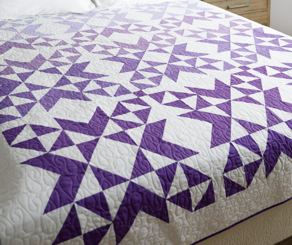A modern quilt featuring a bold geometric pattern in purple and white fabric.