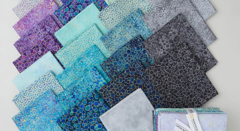 Fat quarters of dots, speckles, and pebbles with metallic accents in shades of cool blue, gray, and lavender. 