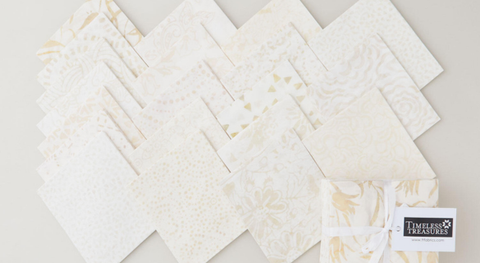 An assortment of fat quarter batik fabric prints with assorted motifs in a tan and white palette.