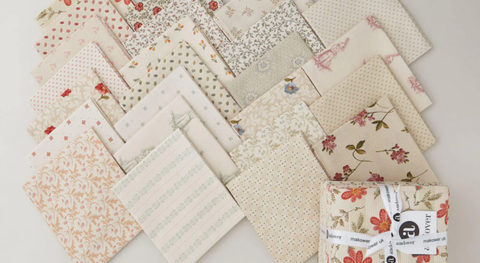 A selection of fat quarter fabrics in a vintage cream palette with pops of light blue and soft red. Prints include flowers, polka dots, and more.